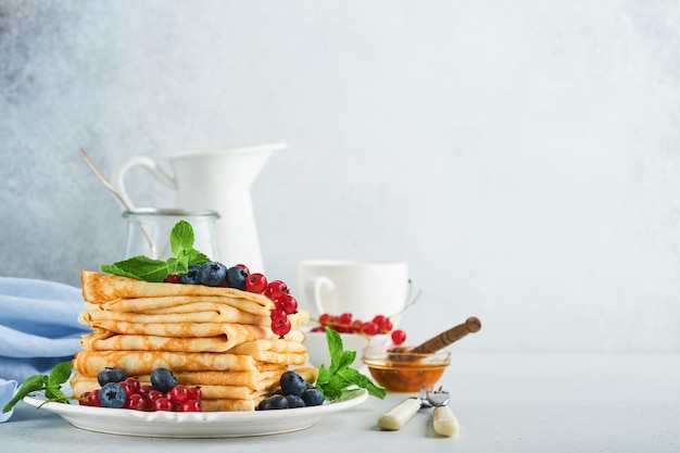 Panqueques Pila de crepes o panqueques finos con bayas arándanos grosellas rojas frambuesas y miel para el desayuno Desayuno casero Copiar espacio Enfoque selectivo