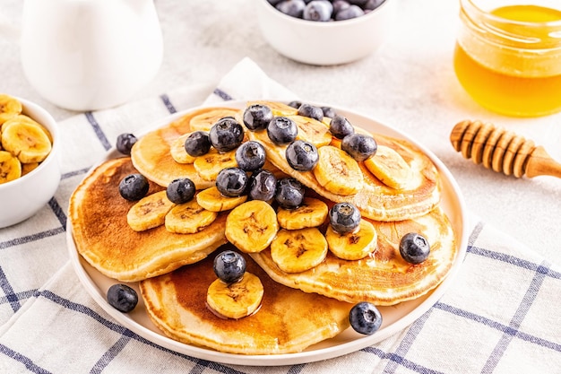 Panqueques con plátano, arándanos en plato blanco, enfoque selectivo.