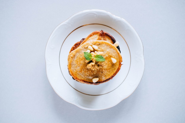 Panqueques de plátano con nueces de cedro y nueces, miel y menta, cucharón de miel sobre un fondo blanco