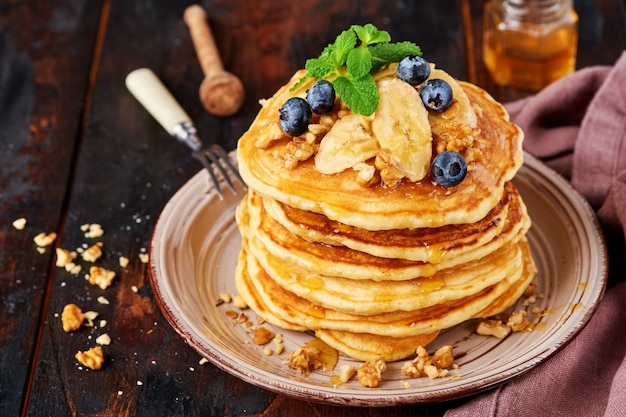 Panqueques con plátano, nuez, miel y caramelo para un desayuno sobre fondo de madera oscura. Enfoque selectivo.