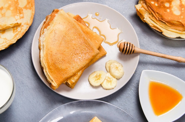 Panqueques con plátanos y miel para el desayuno en la mesa blanca