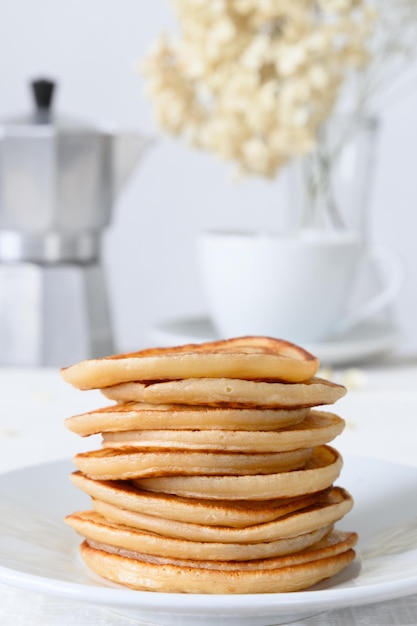 Foto panqueques en plato blanco taza de té y cafetera en mesa blanca