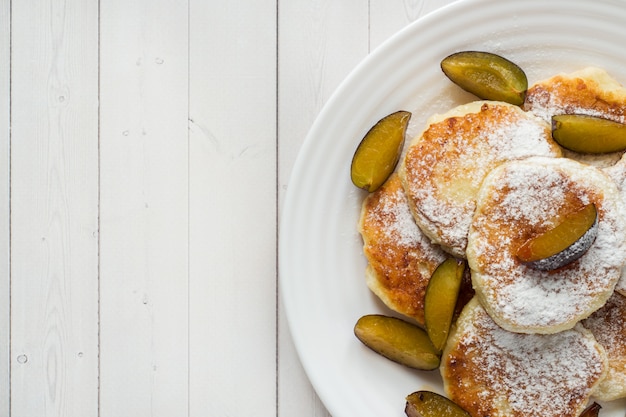 Panqueques de queso en azúcar en polvo con ciruelas frescas en un plato