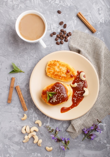 Panqueques de queso con salsa de caramelo en un plato de cerámica color beige y una taza de café en concreto gris