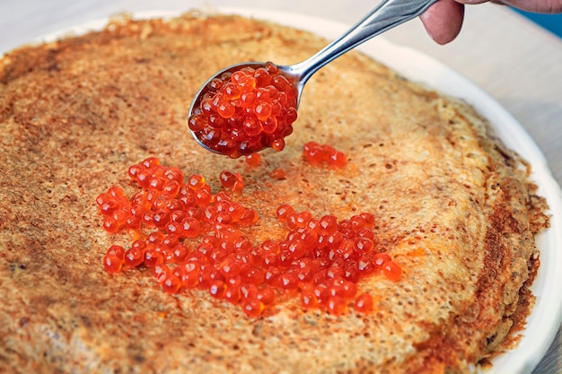 Panqueques recién horneados con caviar rojo sobre placa blanca.