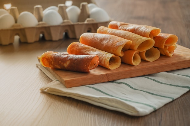 Foto panqueques rellenos con sabores surtidos sobre una tabla de cortar de bambú colocada sobre un paño blanco y rayado sobre una mesa de madera