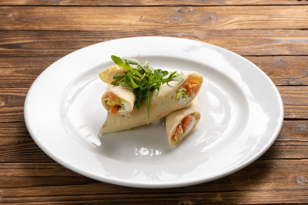 Panqueques rellenos de salmón, queso crema, lechuga y rúcula en un plato de cerámica blanca sobre una mesa de cocina de madera