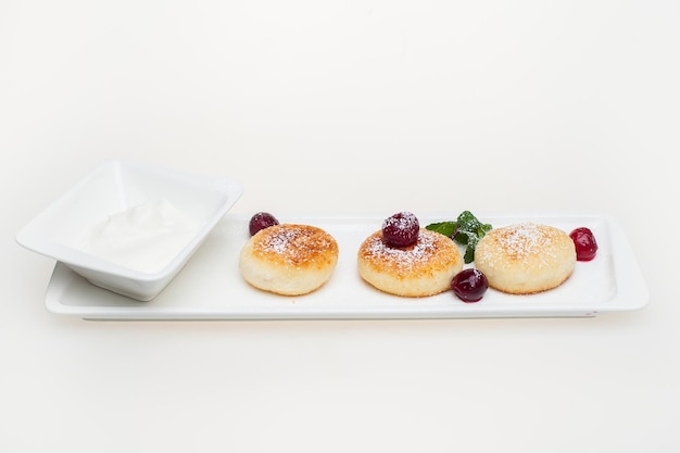 Panqueques de requesón con crema agria y bayas en un plato blanco