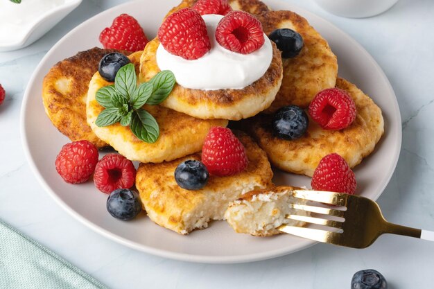 Panqueques de requesón con frambuesas y arándanos sobre fondo claro desayuno o almuerzo