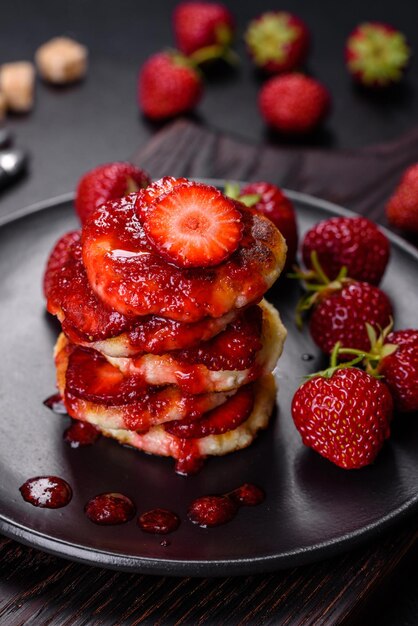 Panqueques de requesón con fresas en rodajas y mermelada de fresa en un plato sobre un fondo de hormigón