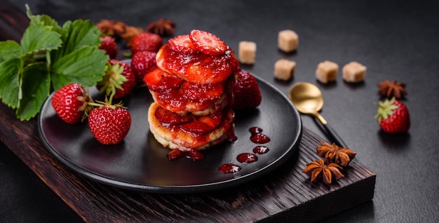 Panqueques de requesón con fresas en rodajas y mermelada de fresa en un plato sobre un fondo de hormigón