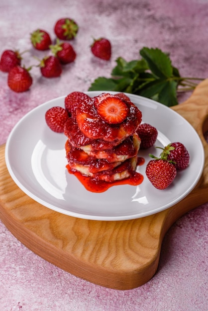 Panqueques de requesón con fresas en rodajas y mermelada de fresa en un plato sobre un fondo de hormigón