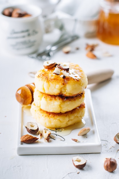 Panqueques de requesón con miel sabrosa y nueces mixtas. Syrniki, buñuelos de cuajada. Fondo blanco