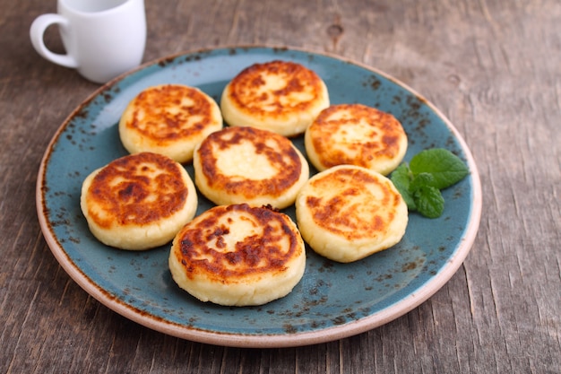 Panqueques de requesón o syrniki en placa azul decorada con menta, vista de cerca. Cocina rusa, ucraniana. Desayuno sabroso y saludable.