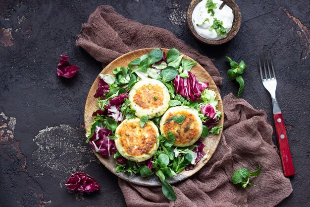 Panqueques de requesón con queso y hierbas servidos con mezcla de ensalada y crema agria.