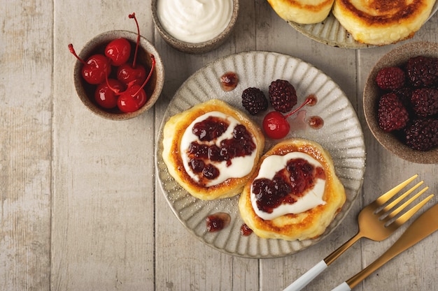 Foto panqueques de requesón, sabrosos buñuelos de cuajada con bayas, crema agria y mermelada, vista superior