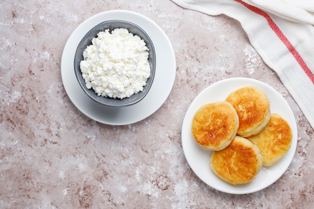 Panqueques de requesón Sirniki o sirniki ruso, buñuelos de requesón o panqueques con un tazón de requesón casero fresco