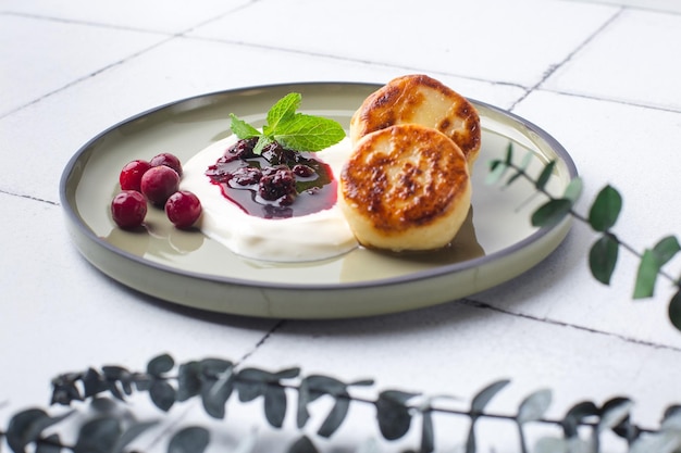 Panqueques de requesón syrniki con bayas frescas y mermelada para el desayuno en el azulejo con eucalipto hig ...