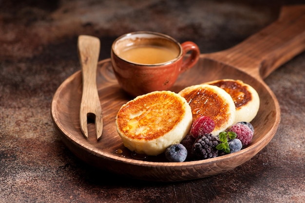 Panqueques de requesón syrniki con miel de bayas y taza de café