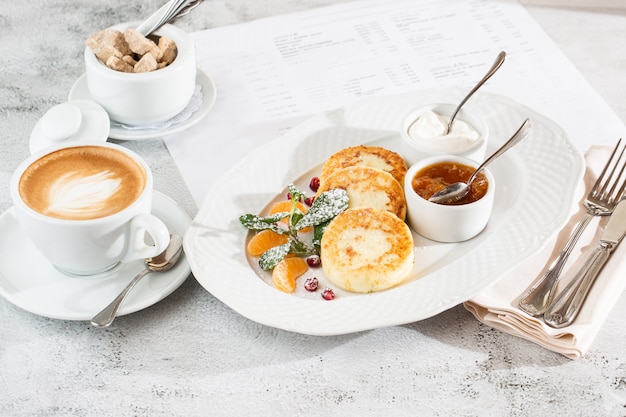 Panqueques de requesón, Syrniki o tartas de queso con crema, miel, menta aislado en mesa de textil blanco Comida hecha en casa. Desayuno sabroso Enfoque selectivo. Foto hotizontal.