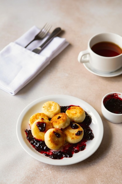 Panqueques de requesón syrniki ricotta buñuelos en plato de cerámica blanca con crema agria y mermelada Desayuno matutino saludable y delicioso Fondo beige Comida para niños