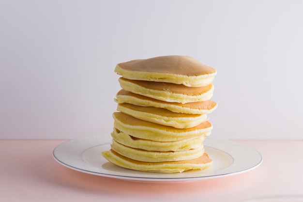 Panqueques sobre fondo rosa blanco Panqueques calientes con miel en un plato blanco Delicioso plato para el desayuno La miel fluye desde un palo de madera sobre panqueques amarillos