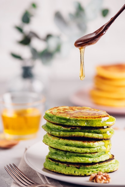 Panqueques verdes con té matcha o espinacas, miel vestida y uvas rojas. Desayuno saludable con superalimentos. Fondo claro, abrazo estilo escandinavo