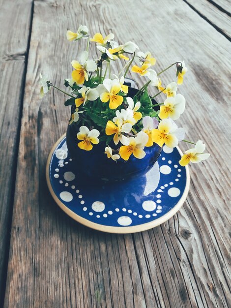 pansy amarelo flores em copo azul na mesa de madeira