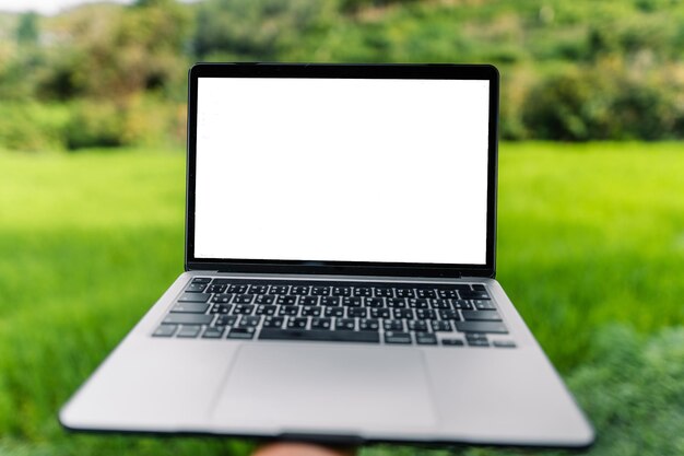 Foto pantalla en blanco de la computadora portátil en una terraza de madera en el fondo de los campos de arroz portátil al aire libre