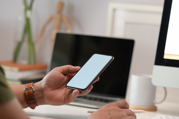 Pantalla en blanco simulacro de teléfono móvil en la mano del hombre en la oficina en casa