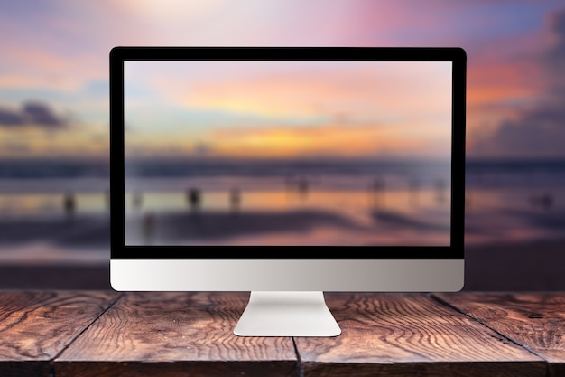 Pantalla de ordenador con imagen borrosa del mar al atardecer en una mesa de madera contra el mismo con bokeh, espacio de copia. Trabajando de forma remota en la costa, en la naturaleza, fuera del concepto de oficina.