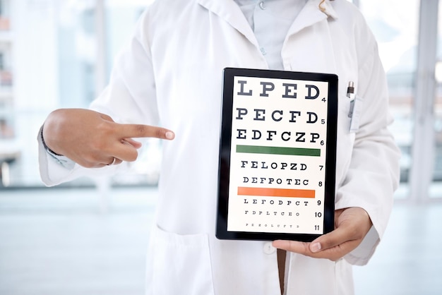 Pantalla de la tableta de manos y tabla optométrica en el hospital para el examen de la vista en la clínica Snellen de atención médica o mujer oftalmóloga o médico que señala la tecnología que muestra letras para la prueba de los ojos