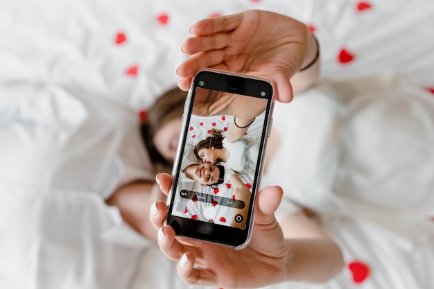 Pantalla del teléfono con selfie de hombre y mujer enamorados besándose en la cama