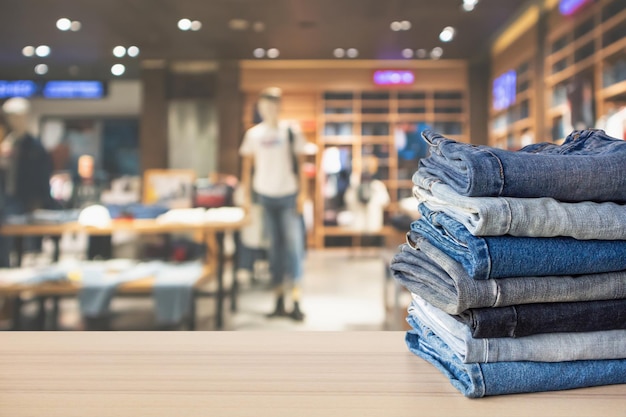 los pantalones vaqueros se apilan en la parte superior de la mesa de madera con una tienda de ropa borrosa abstracta en el fondo del centro comercial