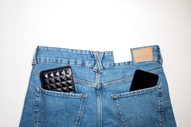 Pantalones vaqueros con una etiqueta de cuero vacía en una cartera de fondo azul y teléfono en el bolsillo trasero
