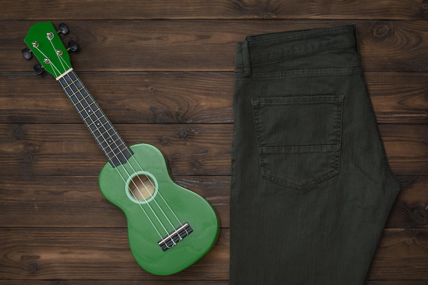 Pantalones vaqueros verdes y un ukelele verde sobre un fondo de madera. Concepto de moda y música folclórica.