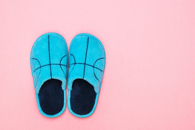 Pantuflas azules con bordado sobre una superficie rosa. Zapatos caseros cómodos