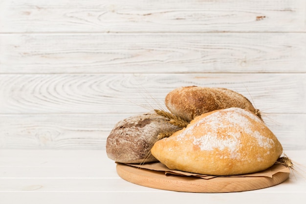 Pão acabado de cozer na tábua contra o fundo branco de madeira vista em perspectiva pão com espaço de cópia