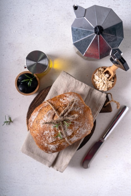 Pão artesanal ciabatta de massa fermentada recém-assada com azeitonas e alecrim em uma mesa abstrata branca