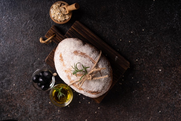 Pão artesanal ciabatta recém-assado com azeitonas e alecrim em uma mesa rústica preta