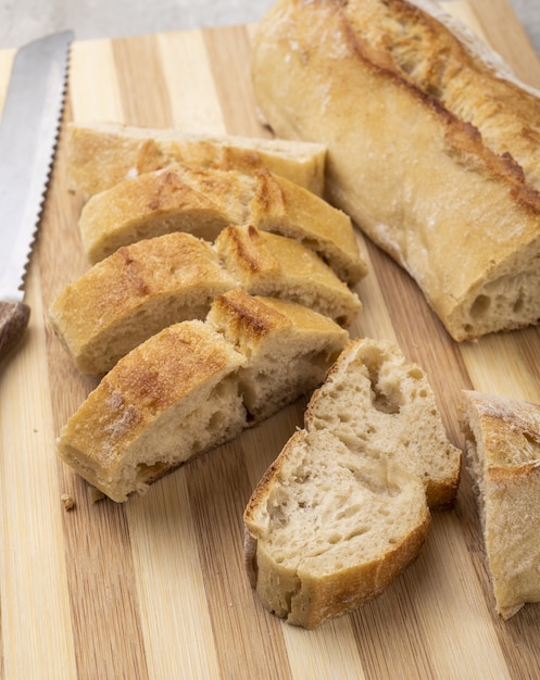 Pão baguete francês caseiro tradicional com fatias sobre tábua de madeira