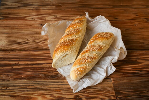 Pão baguete polvilhado com gergelim e papel de embrulho na mesa de madeira