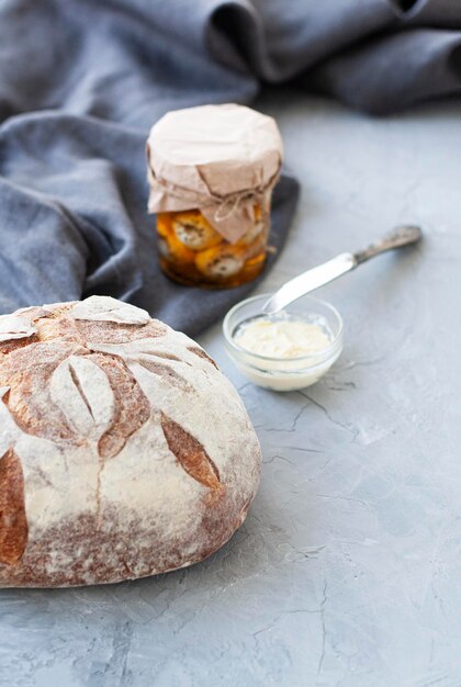 Foto pão caseiro com manteigueira e faca, frasco de vidro em fundo cinza