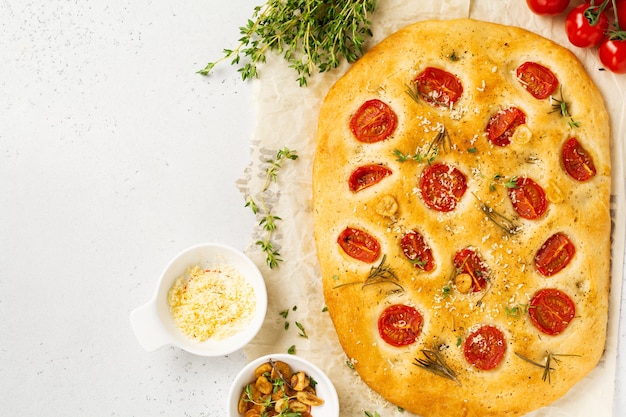 Pão caseiro italiano tradicional assando com tomate cereja, parmesão e alecrim na parede da mesa de luz rústica. Vista do topo.