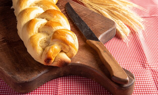 Pão caseiro, dois pães em forma de trança sobre madeira e uma toalha de  mesa quadriculada vermelha e branca, uma faca e um ramo de trigo.