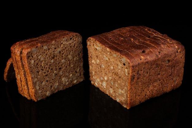 Pão comum com grãos e gergelim cortado em pedaços em um fundo preto. Pão integral