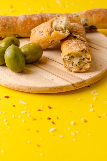 Pão de azeitona italiana na tábua de madeira em fundo amarelo