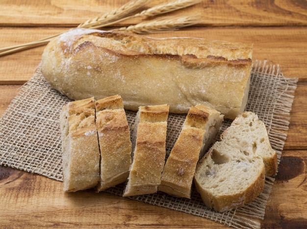 Pão de baguete francês caseiro tradicional com fatias sobre mesa de madeira