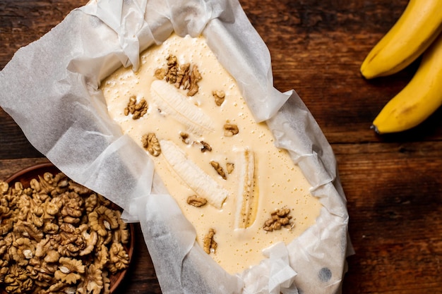 Pão de banana Cozinhar massa crua com banana e nozes em uma assadeira Fundo de madeira Comida vegetariana doce