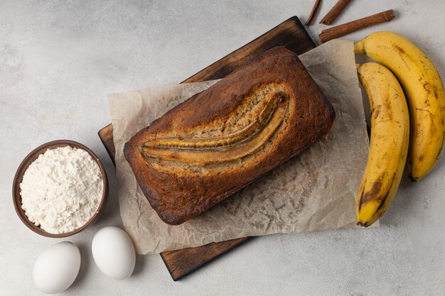 Foto pão de banana fresco pronto em uma assadeira retangular com ingredientes em um fundo claro